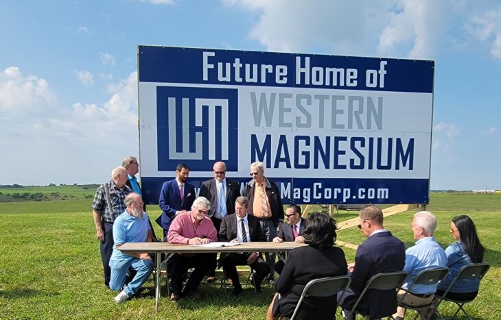 Western Magnesium - primary magnesium production - team members sit in front of a billboard, signing an agreement for the new location of the magnesium plant
