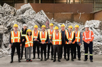Employees in orange vests stand in front of baled aluminum scrap.