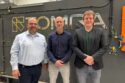 three men stand in front of a TOMRA sorting machine