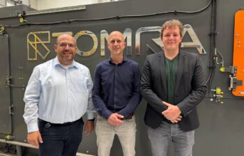 three men stand in front of a TOMRA sorting machine