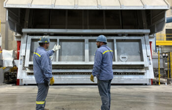 Two men stand in front of a closed aluminum furance.