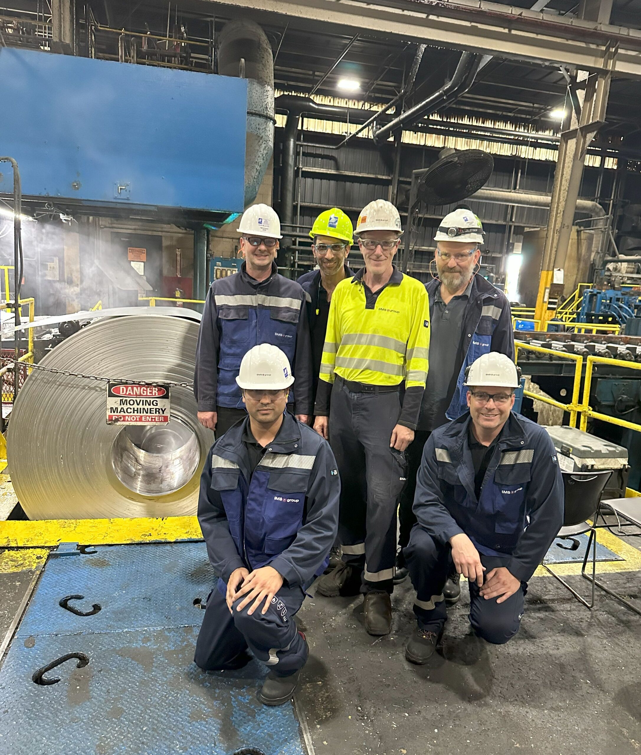 A group of people in protective gear standing by an industrial machine.
