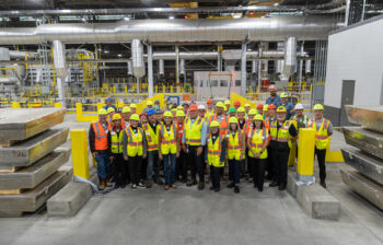 A group of people in safety gear standing in front of casting equipment with large aluminum ingot in the foreground.