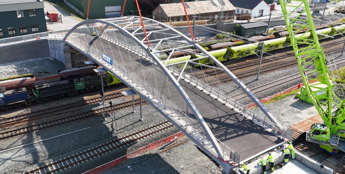 An aluminum bridge being placed into position over railroad tracks via crane