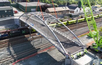 An aluminum bridge being placed into position over railroad tracks via crane