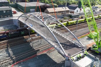 An aluminum bridge being placed into position over railroad tracks via crane