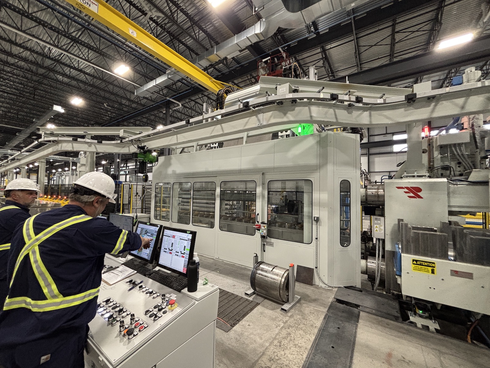 Two employees stand beside a console, observing the extrusion production process.