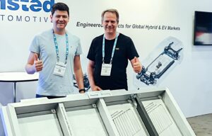 Two men stand in front of an aluminum foam battery housing.