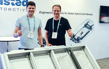 Two men stand in front of an aluminum foam battery housing.