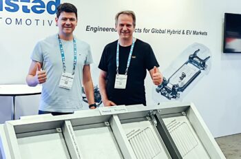 Two men stand in front of an aluminum foam battery housing.
