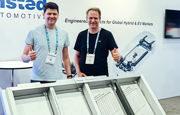 Two men stand in front of an aluminum foam battery housing.