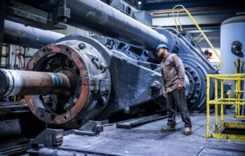 A man peers into the machinery of a piece of industrial equipment.