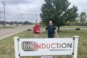 Two men shake hands, while standing by a sign that reads Induction Professionals LLC