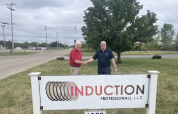Two men shake hands, while standing by a sign that reads Induction Professionals LLC