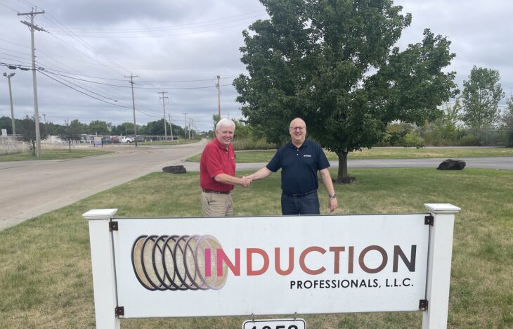 Two men shake hands, while standing by a sign that reads Induction Professionals LLC