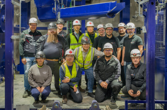 A group of engineers stand next to industrial equipment
