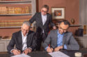 Three men in suits sign a contract