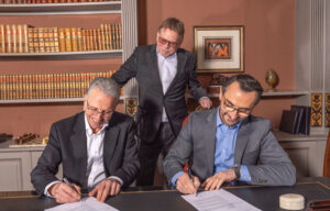 Three men in suits sign a contract