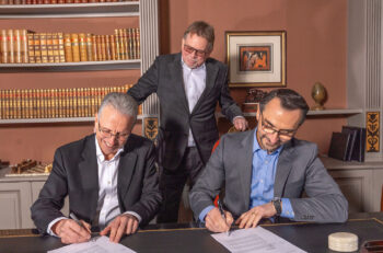 Three men in suits sign a contract