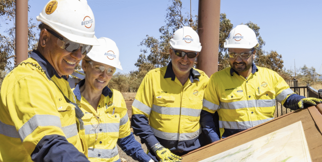 Men stand around a printout of industrial plans