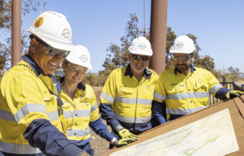 Men stand around a printout of industrial plans