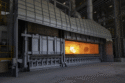 An industrial furnace, with an open door showing orange flames inside.