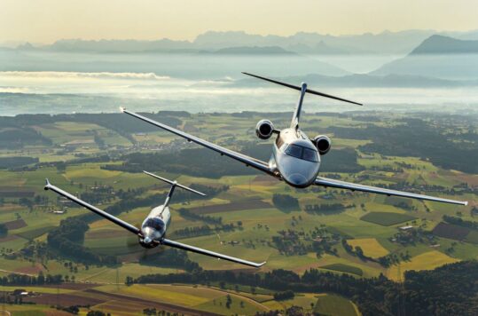 Two aircraft flying over green fields.