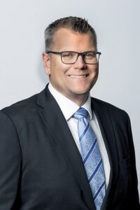 Headshot of a white man with glasses in a suit