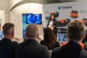 A woman stands at the front of a room talking. Behind her are images of Tomra's sorting equipment.