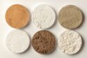 Photo of six pots of rare earth oxides in varying shades of powders.