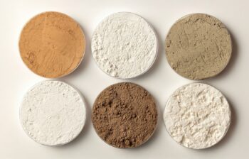 Photo of six pots of rare earth oxides in varying shades of powders.