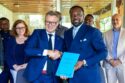 Two men shake hands holding a contract.