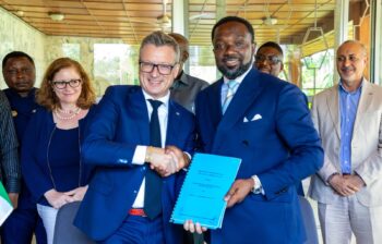 Two men shake hands holding a contract.