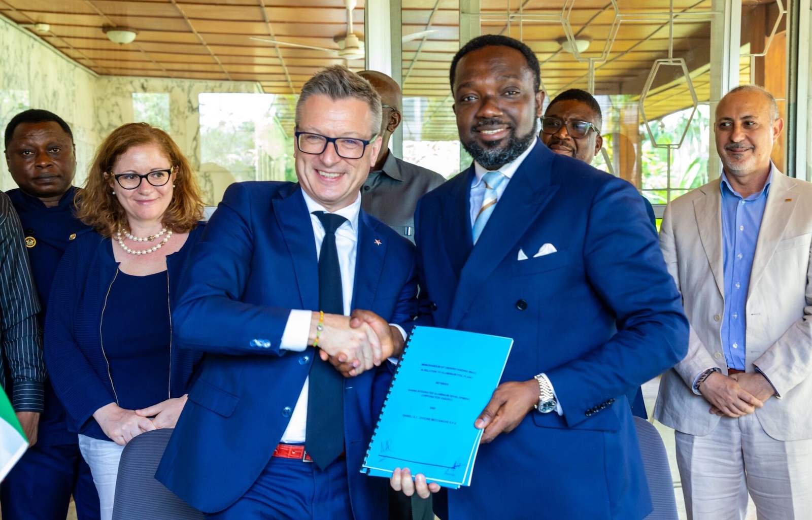 Two men shake hands holding a contract.
