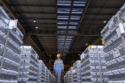 A worker in a yellow hard hat walks between stacks of aluminum ingots.
