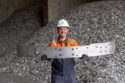 Hydro Cassopolis employee Keith Bonner holding the Cadillac OPTIQ bumper. Piles of aluminum scrap are in the background.
