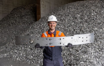 Hydro Cassopolis employee Keith Bonner holding the Cadillac OPTIQ bumper. Piles of aluminum scrap are in the background.