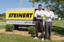 Two men stand next to a sign that read, STEINERT.