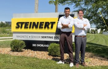 Two men stand next to a sign that read, STEINERT.