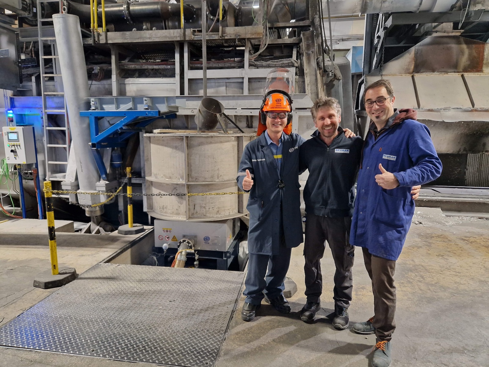 Two men stand beside an industrial furnace